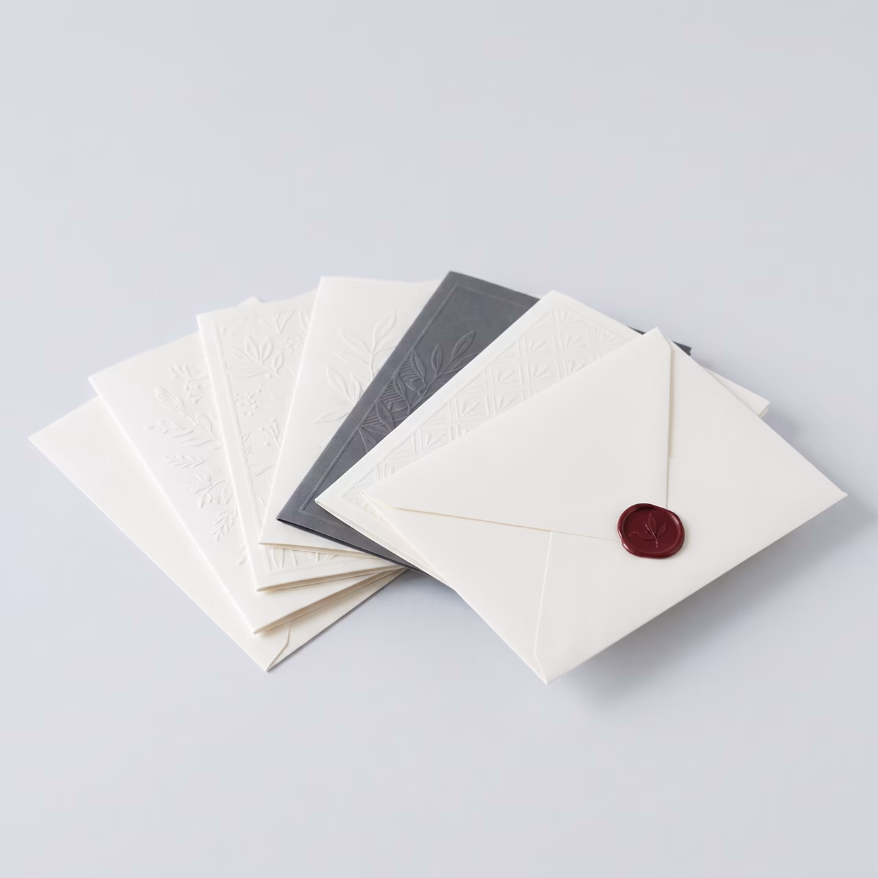 Sammlung eleganter weißer und grauer Umschläge mit Prägungen und rotem Wachssiegel.
